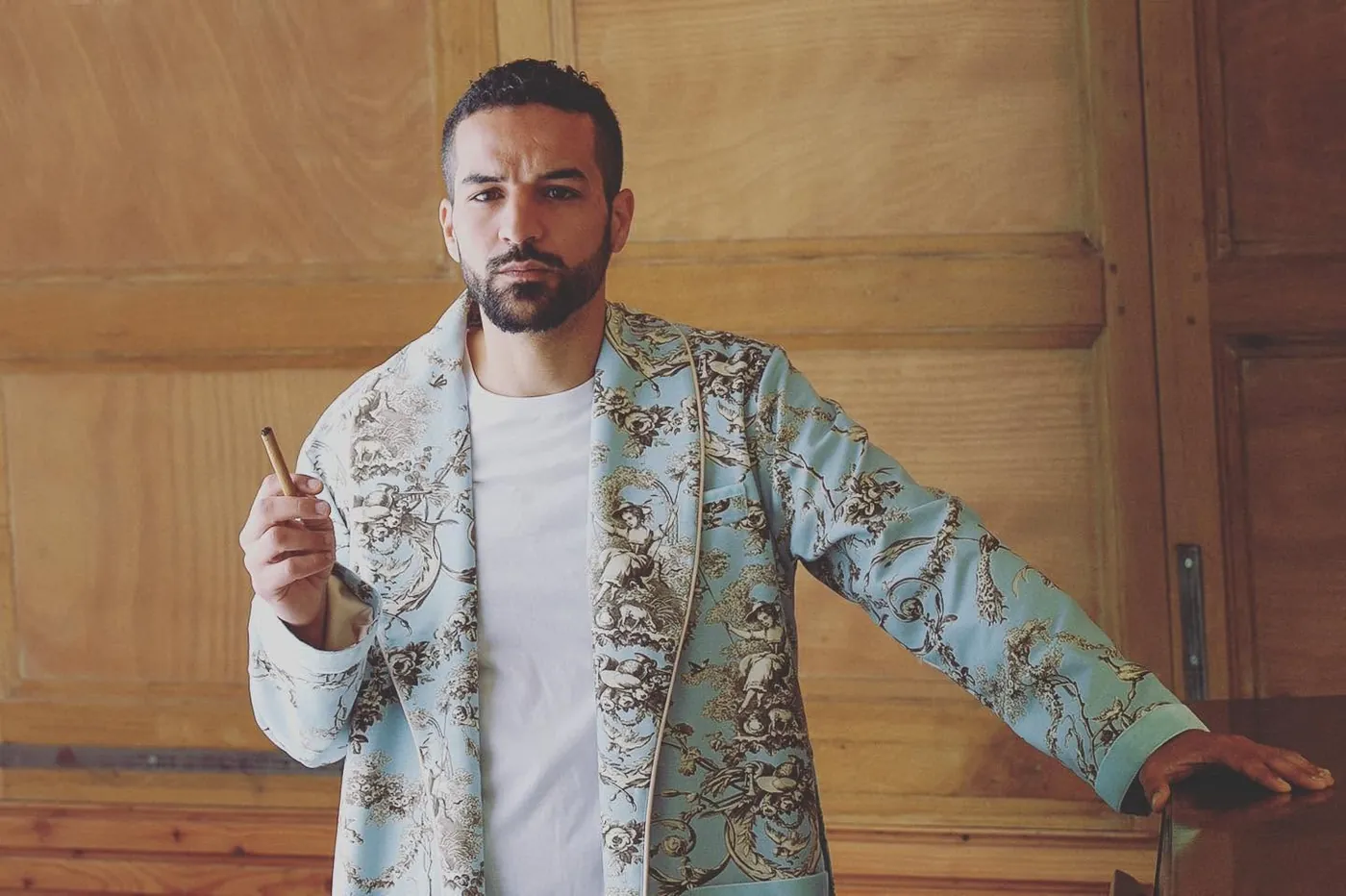 Omar Meftah en veste à motifs, appuyé contre une porte en bois (portrait 2022)