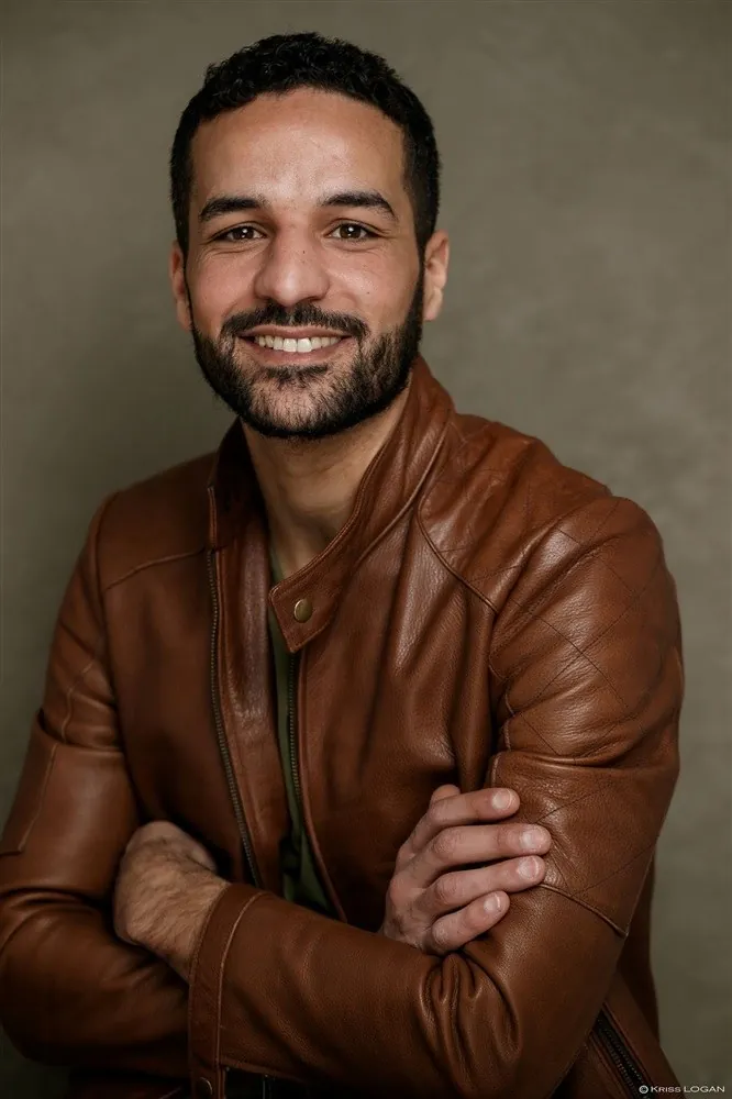 Omar Meftah souriant en veste de cuir marron, bras croisés (portrait 2025)